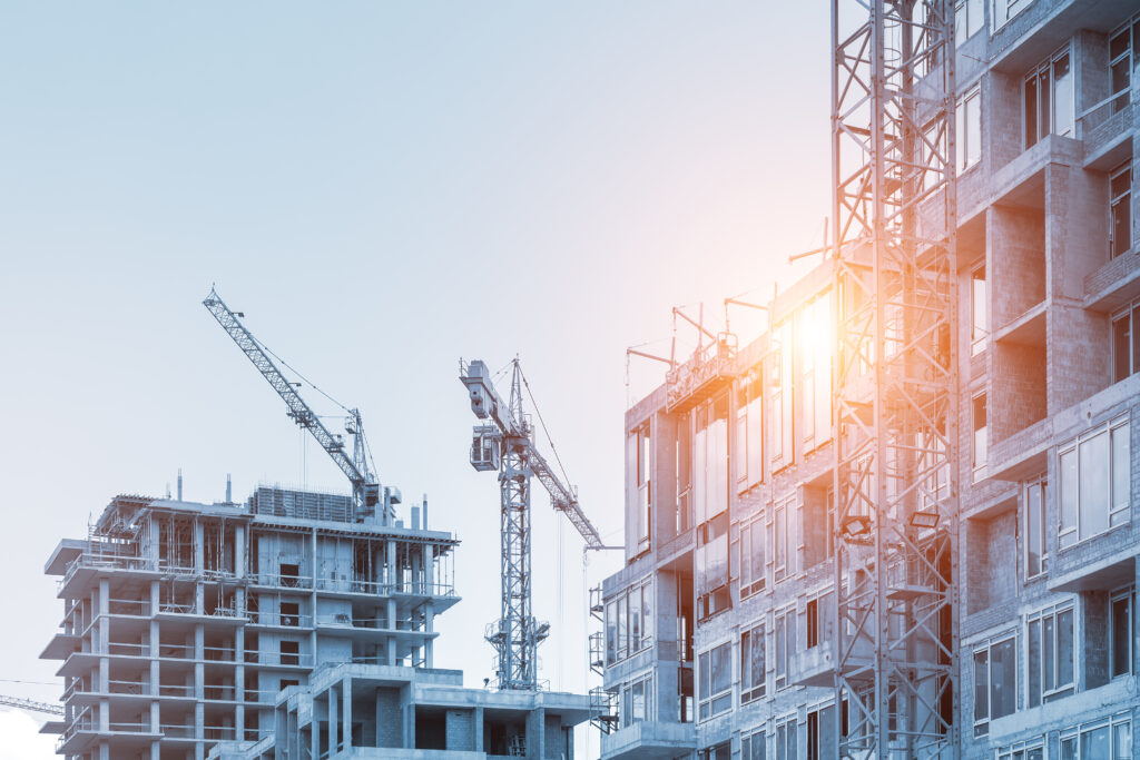 Modern apartment residential building glass facade wall construction site with many high tower cranes and heavy machinery against blue sky background. Industrial scenic urban city development project.