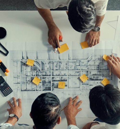 Top down aerial view of interior designer writing at sticky note while planning design with engineer team. Group of diverse architect and skilled manager looking building construction. Alimentation.